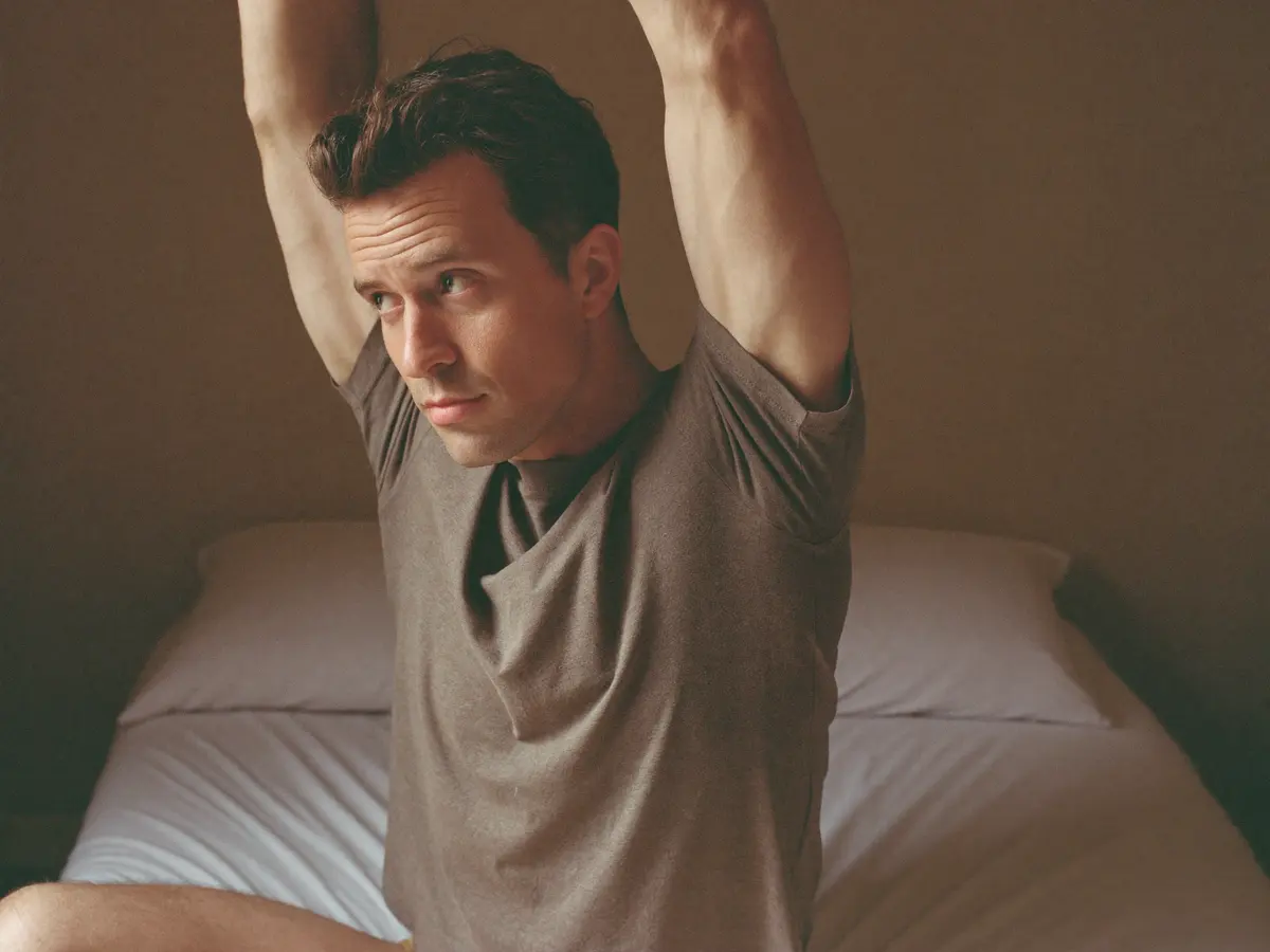 Man stretching on the edge of his bed in morning light